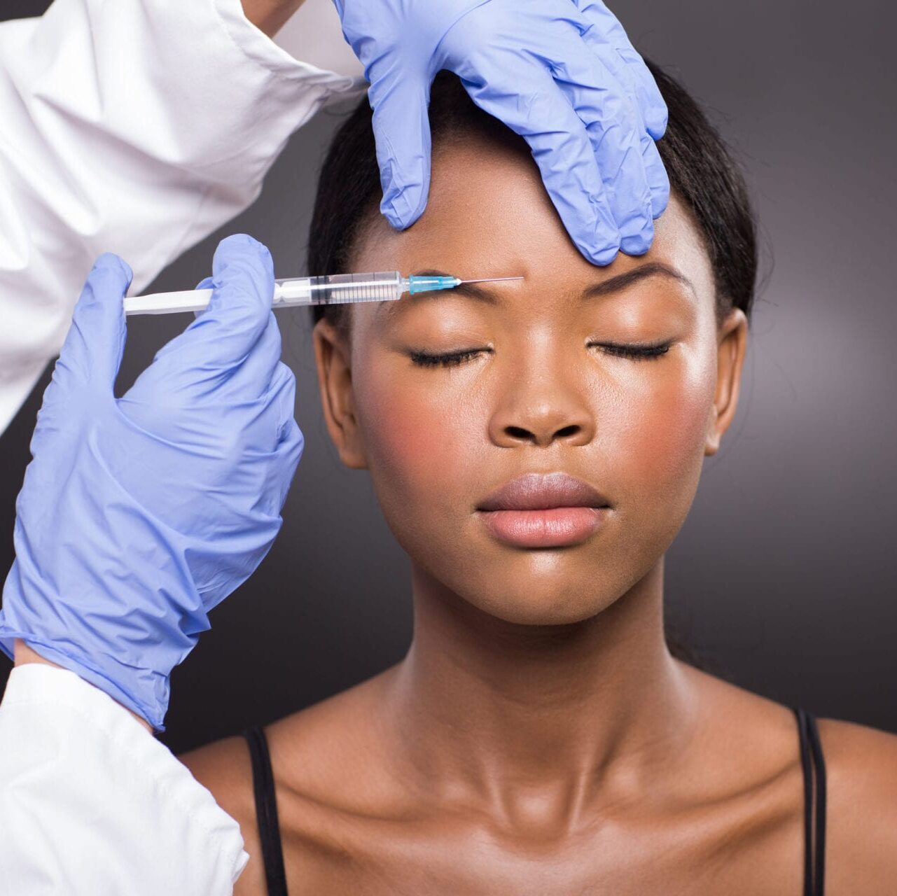 close up of cosmetic doctor injecting african woman forehead